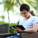 Ein junger Mann sitzt auf dem Sessel mit einem Tablet in der Hand