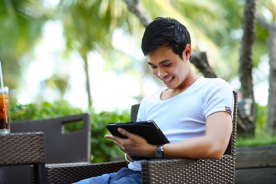 Ein junger Mann sitzt auf dem Sessel mit einem Tablet in der Hand